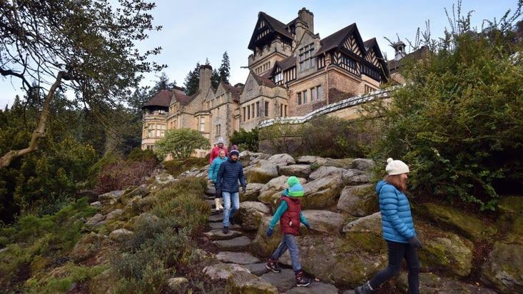 A group of visitors are walk down large stone steps in the Rock Garden on a winter's day. Cragside House is in the background.